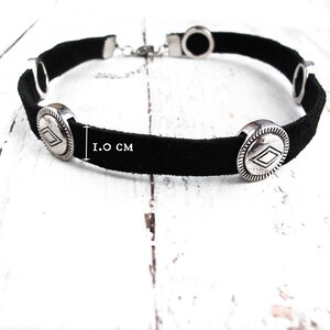 May include: Black suede choker necklace with silver-toned metal accents. The necklace features four round charms with a diamond-shaped design. The choker is 1.0 inches wide.