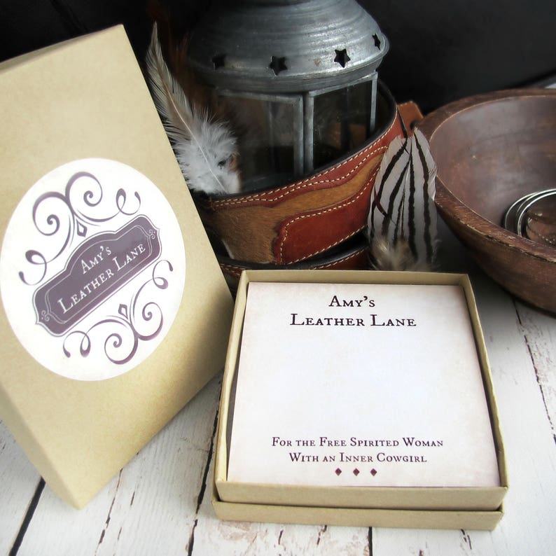 May include: A brown box with a white sticker that says "Amy's Leather Lane" and a white card with the same text and the words "For the Free Spirited Woman With an Inner Cowgirl".