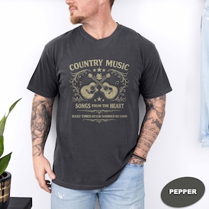 May include: Pepper-colored t-shirt featuring a country music design. The graphic includes two guitars, stars, and the text "Country Music Songs from the Heart. Hard Times Never Sounded So Good."