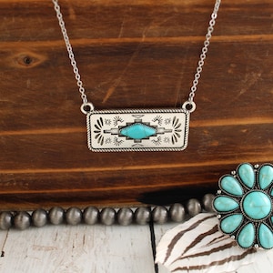 May include: A silver necklace with a turquoise stone set in a rectangular pendant featuring a southwestern design.