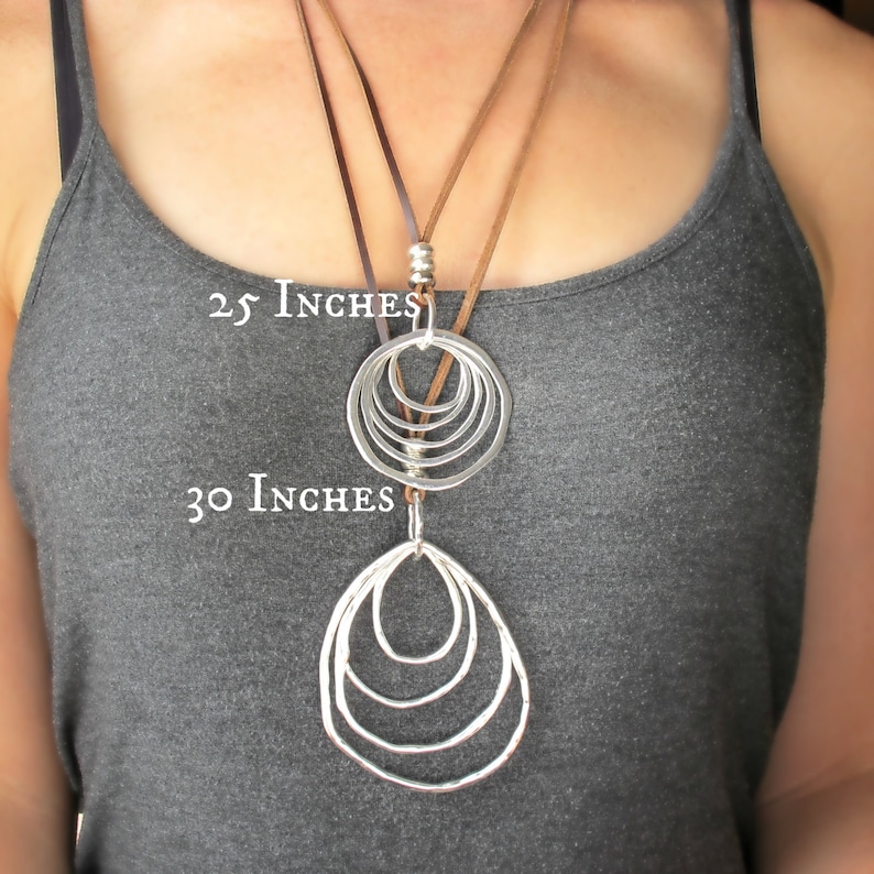 May include: A silver necklace with two pendants, one with five overlapping circles and the other with five overlapping ovals. The necklace is on a brown leather cord and is available in two lengths: 25 inches and 30 inches.