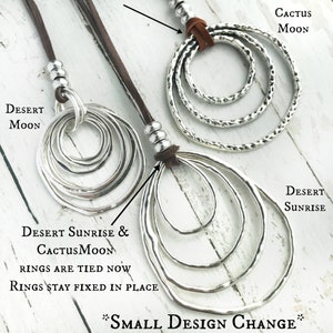 May include: Two silver circle pendant necklaces with brown leather cords. The necklaces feature multiple circles of varying sizes. The text "DESERT SUNRISE & CACTUSMOON RINGS ARE TIED NOW RINGS STAY FIXED IN PLACE *SMALL DESIGN CHANGE*" is visible below the necklaces.