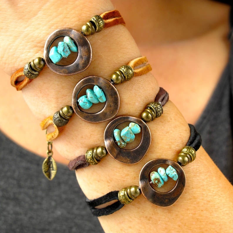May include: Four leather bracelets with turquoise stones set in copper circles. Each bracelet has a different color of leather: brown, tan, black, and brown. The bracelets are stacked on a person's wrist.