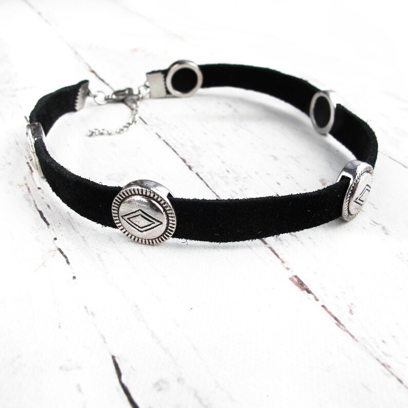 May include: Black suede choker necklace with silver-toned metal accents. The accents feature a geometric diamond shape.