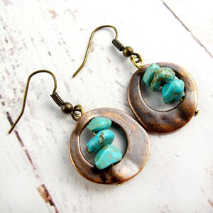 May include: A pair of copper hoop earrings with turquoise stones hanging from them. The earrings have a rustic, bohemian style.