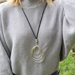 May include: A silver necklace with a pendant made of three interlocking oval shapes. The necklace is on a black cord and is worn by a person wearing a gray sweater.