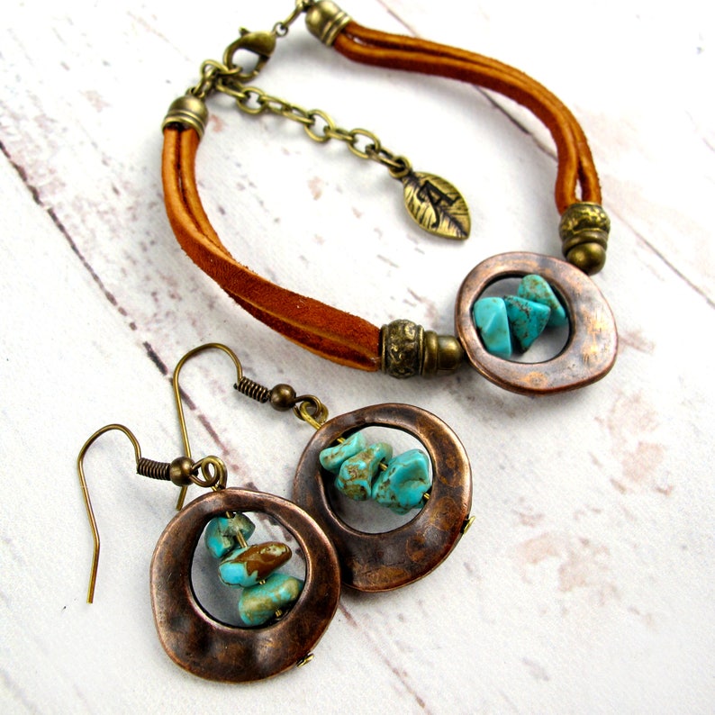 May include: A set of turquoise and copper jewelry featuring a leather bracelet with a copper circle pendant and matching earrings. The pendant and earrings have turquoise stones set in a copper frame.