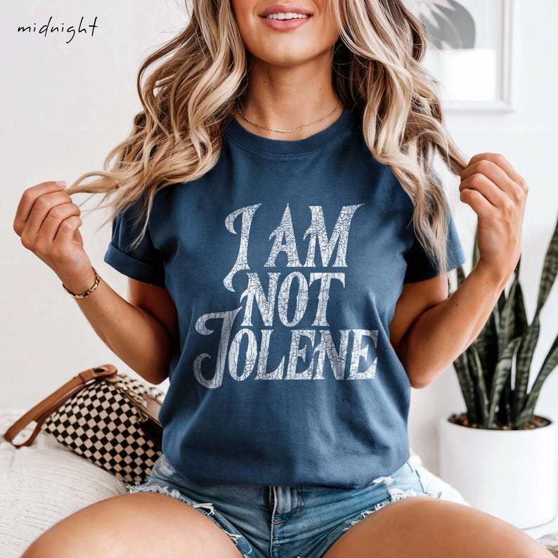 Pu&ograve; includere: Una maglietta blu navy con la scritta "I AM NOT JOLENE" in un carattere bianco invecchiato. La maglietta ha maniche corte e girocollo. La parola "midnight" &egrave; nell'angolo in alto a sinistra.