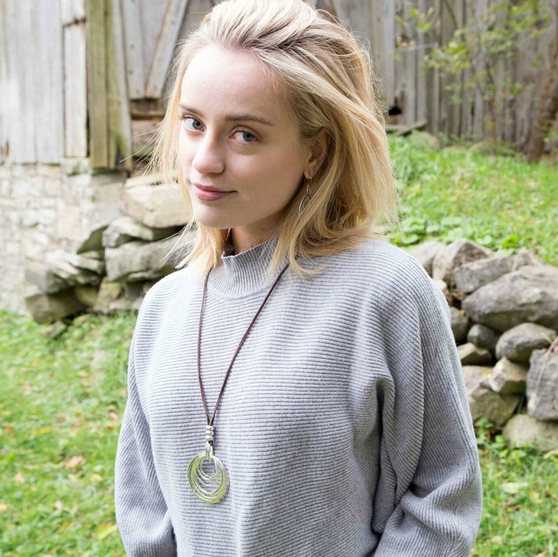 May include: A woman wearing a gray sweater with a long silver necklace featuring a circular pendant. The necklace is made of multiple overlapping circles.