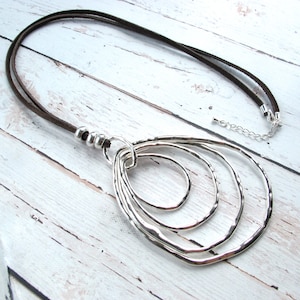 May include: A brown leather cord necklace with a silver pendant featuring five interlocking circles. The pendant is hammered and has a textured finish.