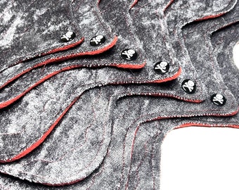 May include: A stack of reusable cloth menstrual pads. The pads are gray with a textured pattern, red trim, and skull and crossbones snaps. The pads are layered on top of each other.