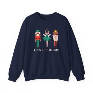 May include: Navy blue sweatshirt with a Christmas-themed graphic featuring a nutcracker, a ballerina, and a mouse. The text "Let's Get Crackin'" is printed below the graphic.
