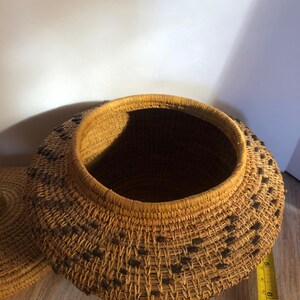 May include: A round, woven basket with a lid. The basket is made of natural-colored fibers with a darker pattern of small, square accents. The rim and lid edge are reinforced with a darker, thicker weave. The basket is approximately 8 inches in diameter.