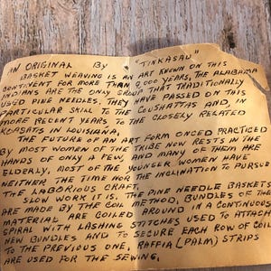 May include: A handwritten note on aged paper, detailing the history of "Tinkasau" basket weaving. The text describes the art form's origins with the Alabama Indians, the use of pine needles, and the coil method.