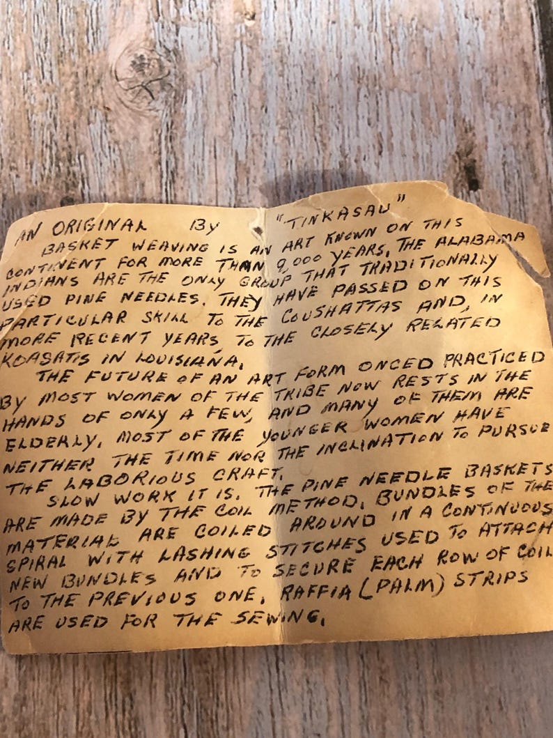 May include: A handwritten note on aged paper, detailing the history of "Tinkasau" basket weaving. The text describes the art form's origins with the Alabama Indians, the use of pine needles, and the coil method.