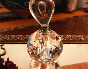 May include: A clear glass bottle with a faceted design and a crystal stopper. The bottle is sitting on a mirrored surface with a gold frame.