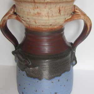 May include: A ceramic vase with two handles, featuring a brown, blue, and white glaze. The vase has a wide mouth and a rounded body.