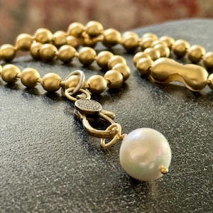 May include: A gold chain necklace with a large pearl pendant. The chain is made of small, round beads and has a clasp with a small diamond accent.