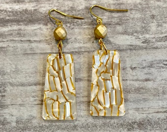 May include: A pair of gold earrings with white rectangular dangles. The dangles have a gold crackle pattern.