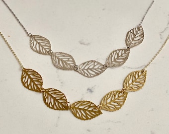 May include: Two delicate necklaces with leaf-shaped pendants. One necklace is gold and the other is silver.