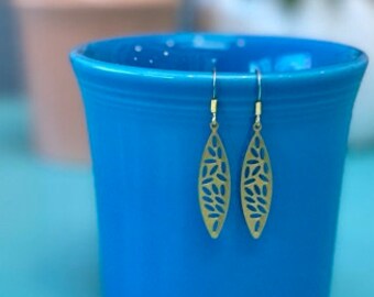 May include: A pair of gold-toned dangle earrings with a leaf design. The earrings are hanging from a blue ceramic planter.