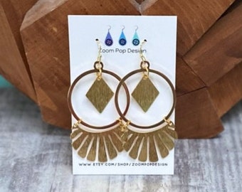 May include: Gold hoop earrings with a diamond-shaped pendant and a fan-shaped design. The earrings are on a white card with the text "Zoom Pop Design" and a website address.