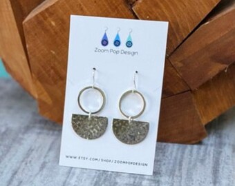 May include: Silver earrings with a hammered half-circle design and a silver hoop. The earrings are on a white card with the text "Zoom Pop Design" and a website address.