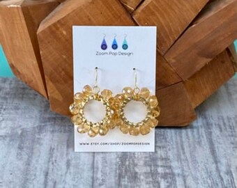 May include: A pair of gold hoop earrings with a circle of clear amber beads. The earrings are on a white card with the text "Zoom Pop Design" and a website address.
