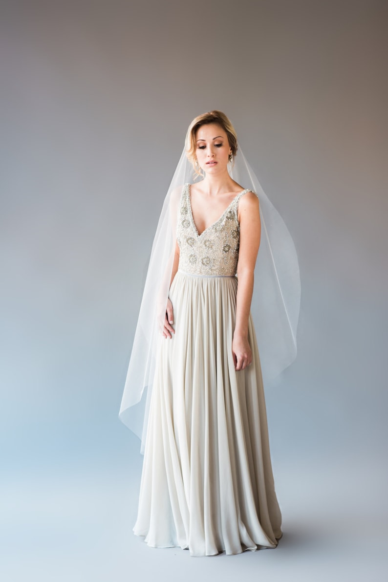 May include: A bride wearing a white wedding dress with a beaded bodice and a flowing skirt. She is wearing a veil and has her hair pulled back.