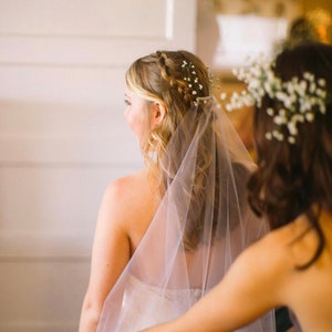 May include: A bride with a white veil and a floral crown is having her veil adjusted by a bridesmaid.
