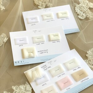 May include: A white card with swatches of different colored tulle fabric. The swatches are labeled with the color names: White, Light Ivory, Dark Ivory, Champagne, Blush, and Pink. The card also includes the text "Yuri C." and "Morbido Tulle - Light Ivory".