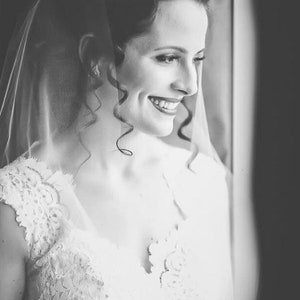 May include: A bride wearing a white lace wedding dress with a veil. She is smiling and looking to the side.