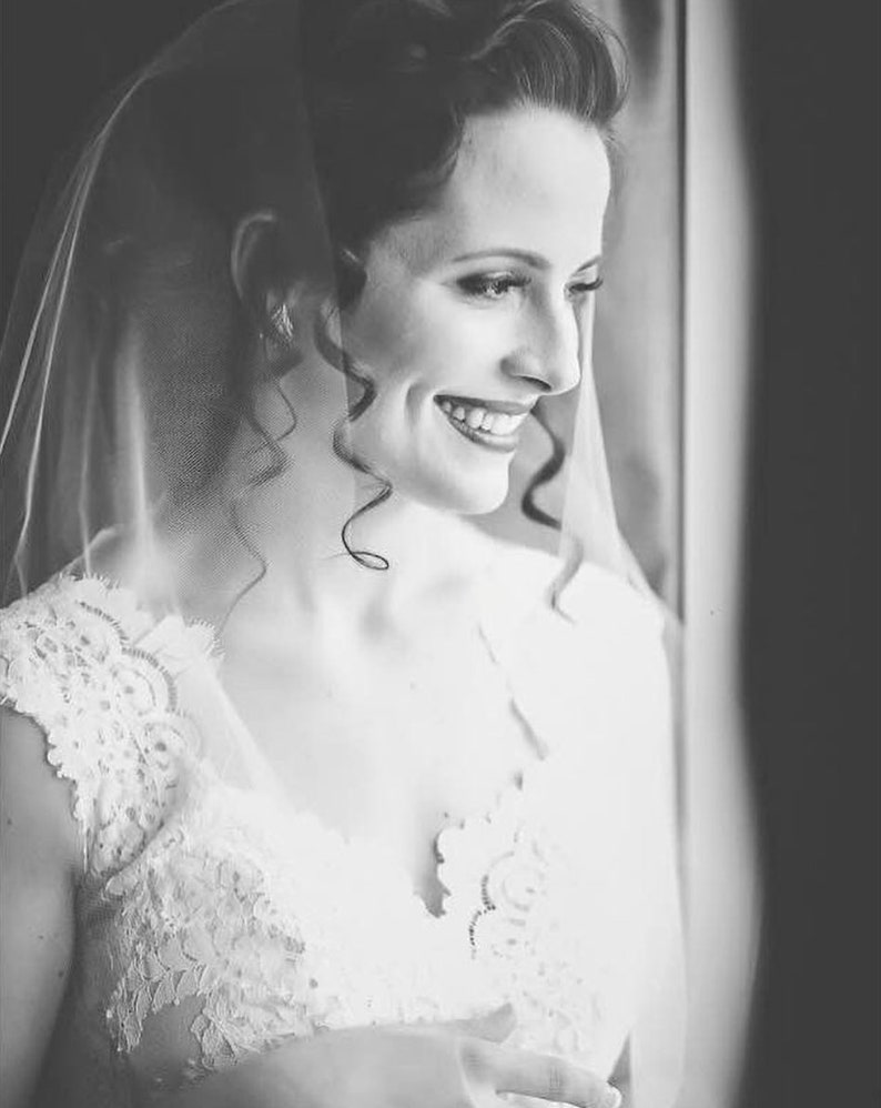 May include: A bride wearing a white lace wedding dress with a veil. She is smiling and looking to the side.