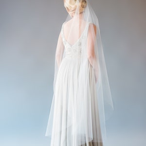 May include: A white wedding dress with a long veil. The dress has a V-neckline and a fitted bodice. The skirt is flowing and has a slight train.