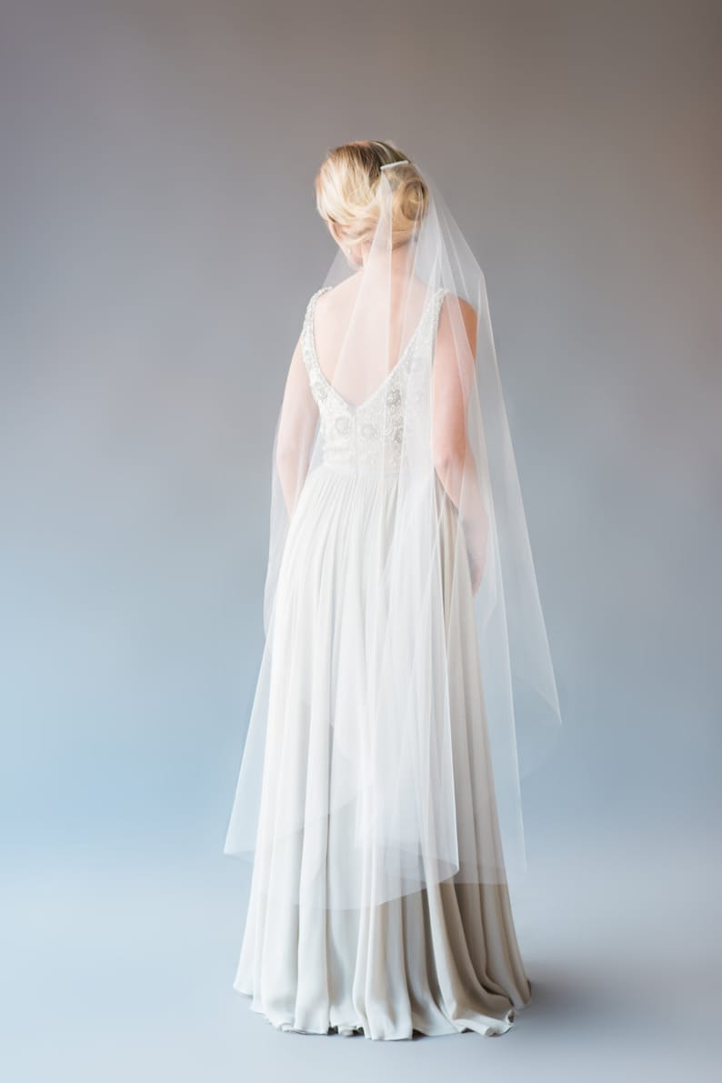 May include: A white wedding dress with a long veil. The dress has a V-neckline and a fitted bodice. The skirt is flowing and has a slight train.