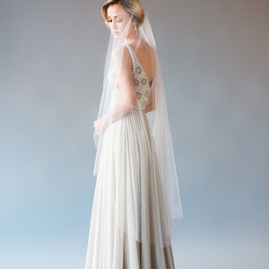 May include: A bride wearing a white wedding dress with a beaded bodice and a long veil. The dress has a flowing skirt and the bride is looking down.