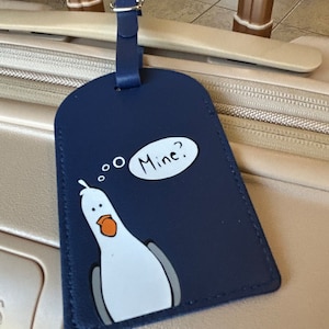 以下が含まれることがあります： 白い漫画の海鳥と「...o Mine?」という吹き出しが書かれた青い荷物タグ