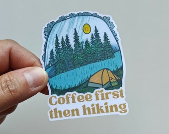 Könnte beinhalten: Ein Aufkleber mit einer blauen und grünen Illustration einer Waldszene mit einem Zelt und dem Text "Coffee first then hiking".