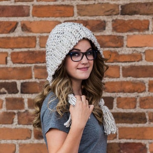 Könnte beinhalten: Eine Häkelmütze mit Kapuze und einem langen Schal. Mütze und Schal sind weiß mit schwarzen Flecken. Das Model trägt die Mütze und den Schal und schaut in die Kamera. Der Text "CROCHET PATTERN from Made with a Twist" befindet sich am unteren Rand des Bildes.