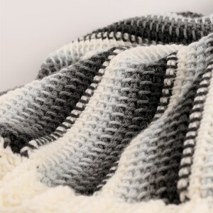 May include: A close-up of a crocheted blanket with a striped pattern in shades of white, gray, and black.