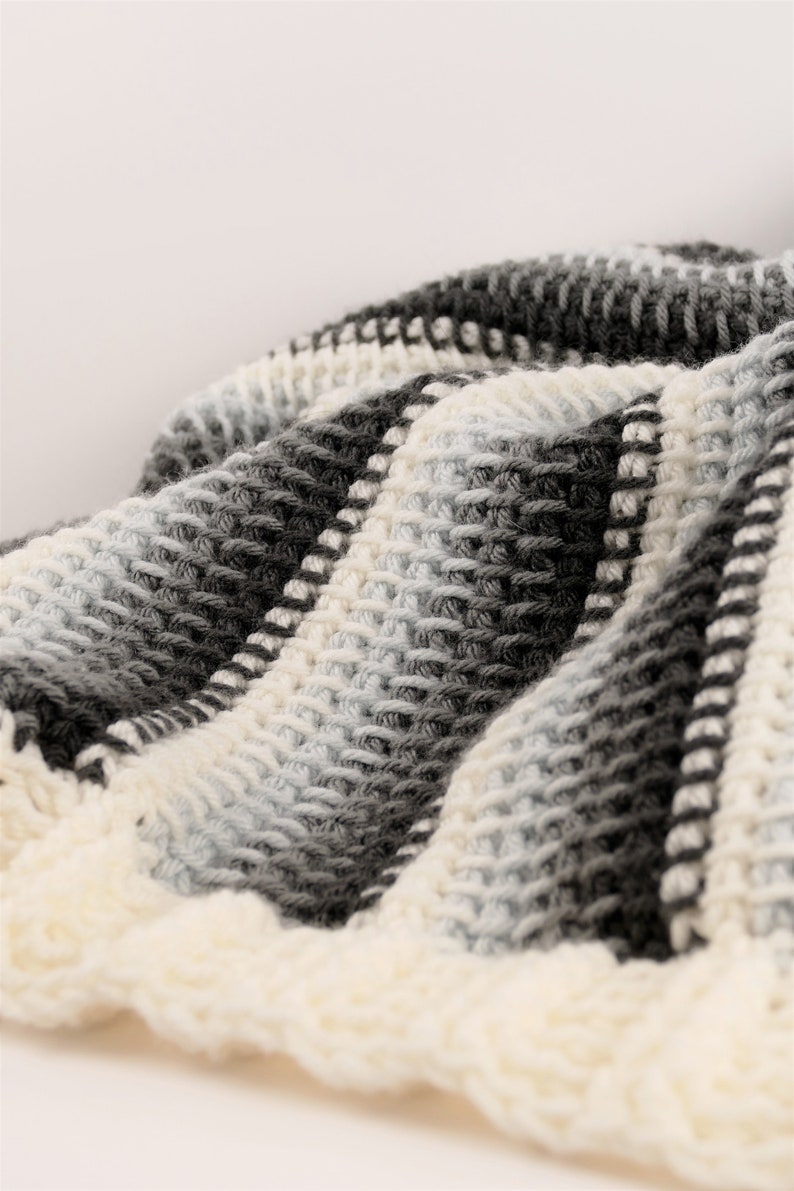 May include: A close-up of a crocheted blanket with a striped pattern in shades of white, gray, and black.