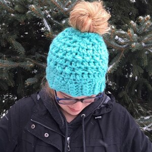 Peut inclure: Un bonnet en crochet bleu turquoise avec un trou au sommet pour un chignon.