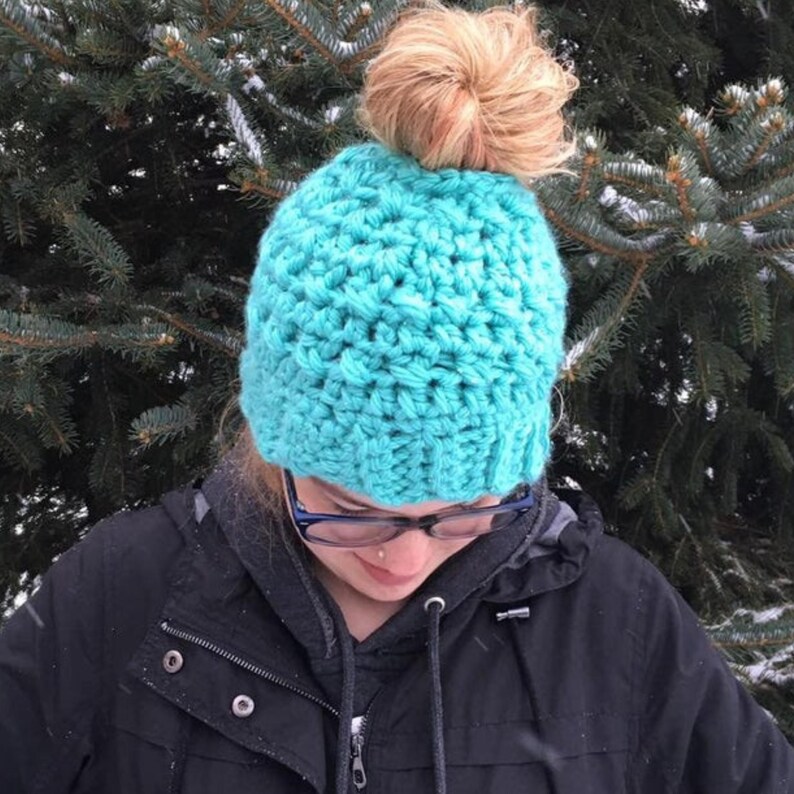 Peut inclure: Un bonnet en crochet bleu turquoise avec un trou au sommet pour un chignon.