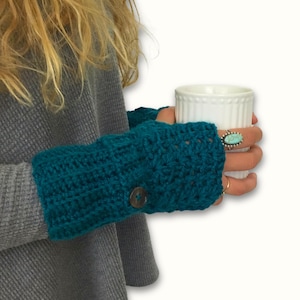 May include: Teal blue crocheted fingerless gloves with a button detail. The gloves are worn by a person holding a white mug.