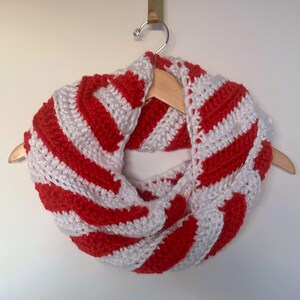 Peut inclure: &Eacute;charpe infinie crochet&eacute;e &agrave; la main, ray&eacute;e rouge et blanche. Le motif ray&eacute; est r&eacute;p&eacute;t&eacute;. L'&eacute;charpe est pr&eacute;sent&eacute;e sur un cintre en bois. Le fil &eacute;pais donne un aspect textur&eacute; et chaleureux, parfait pour l'hiver.