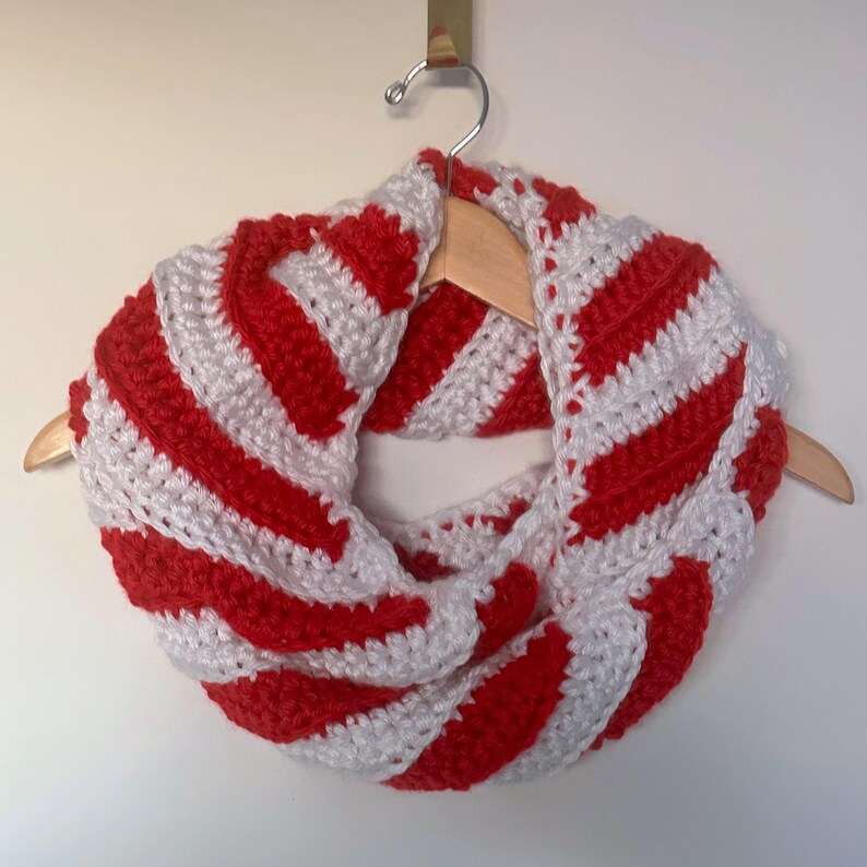 Peut inclure: &Eacute;charpe infinie crochet&eacute;e &agrave; la main, ray&eacute;e rouge et blanche. Le motif ray&eacute; est r&eacute;p&eacute;t&eacute;. L'&eacute;charpe est pr&eacute;sent&eacute;e sur un cintre en bois. Le fil &eacute;pais donne un aspect textur&eacute; et chaleureux, parfait pour l'hiver.