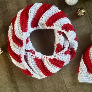 Peut inclure: &Eacute;charpe infinie faite &agrave; la main, crochet&eacute;e avec des rayures rouges et blanches en spirale. L'&eacute;charpe est circulaire et semble douce et chaude. Des d&eacute;corations de No&euml;l sont en arri&egrave;re-plan.