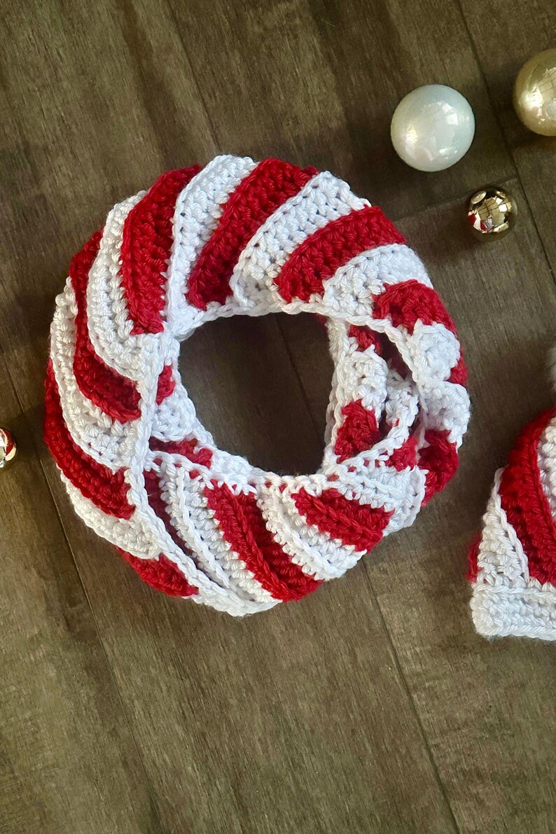 Peut inclure: &Eacute;charpe infinie faite &agrave; la main, crochet&eacute;e avec des rayures rouges et blanches en spirale. L'&eacute;charpe est circulaire et semble douce et chaude. Des d&eacute;corations de No&euml;l sont en arri&egrave;re-plan.