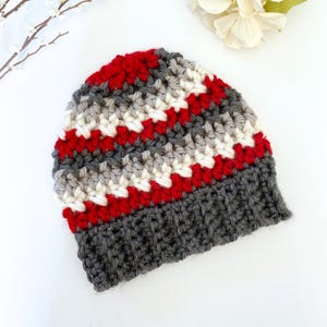 Peut inclure: Un bonnet en crochet ray&eacute; gris, blanc et rouge avec un bord gris.