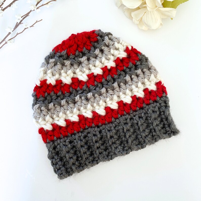 Peut inclure: Un bonnet en crochet ray&eacute; gris, blanc et rouge avec un bord gris.